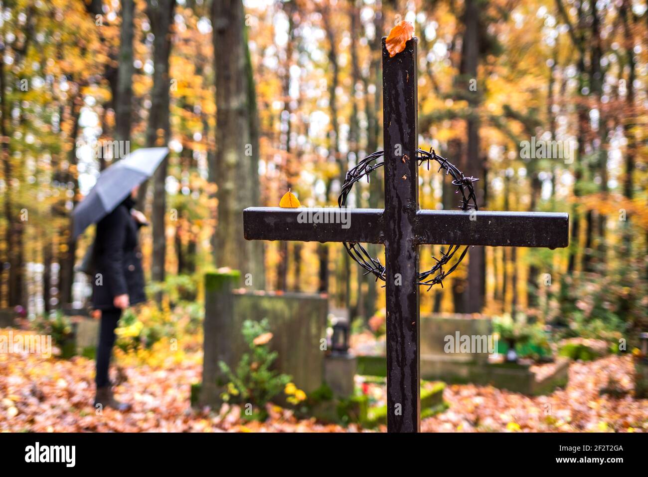 Religious cross in cemetery. Mourning woman in black standing next to tombstoneat graveyard  in rain. Silent memory for dead relatives Stock Photo