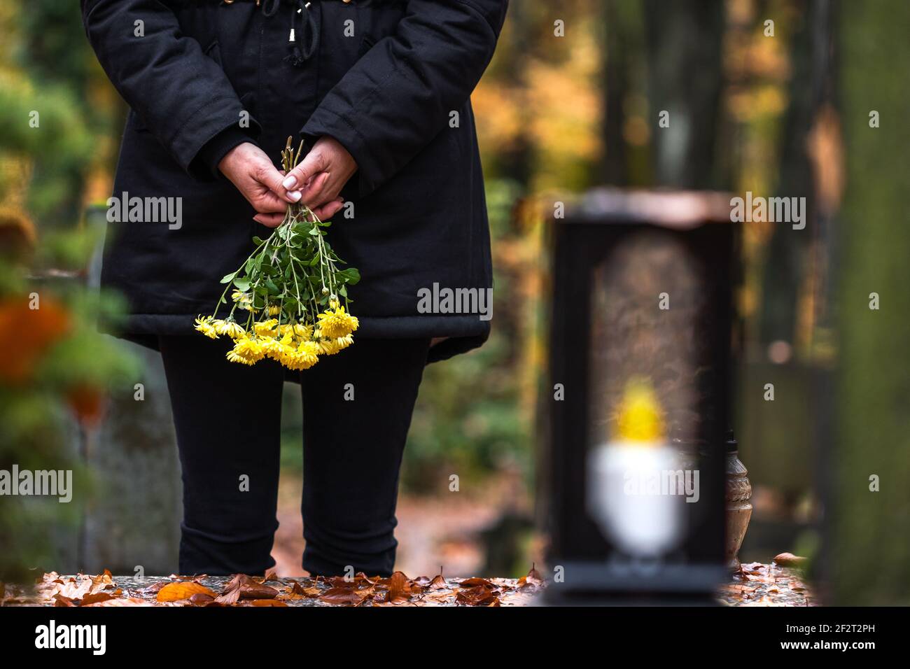 Mourning woman holding flowers in hands and standing at grave in ...