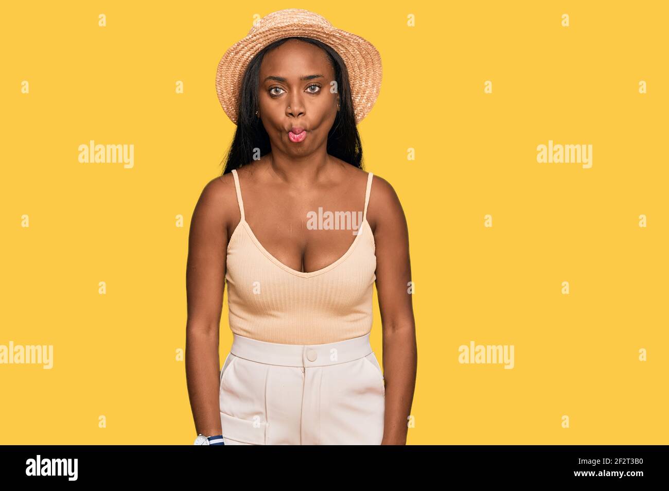 Young black woman wearing summer hat making fish face with lips