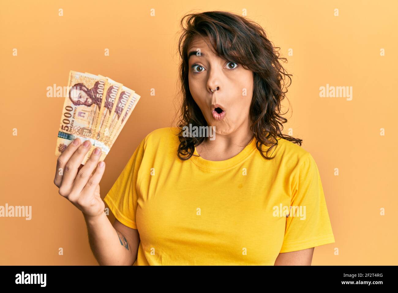Young Hispanic Woman Holding 5000 Hungarian Forint Banknotes Scared And Amazed With Open Mouth