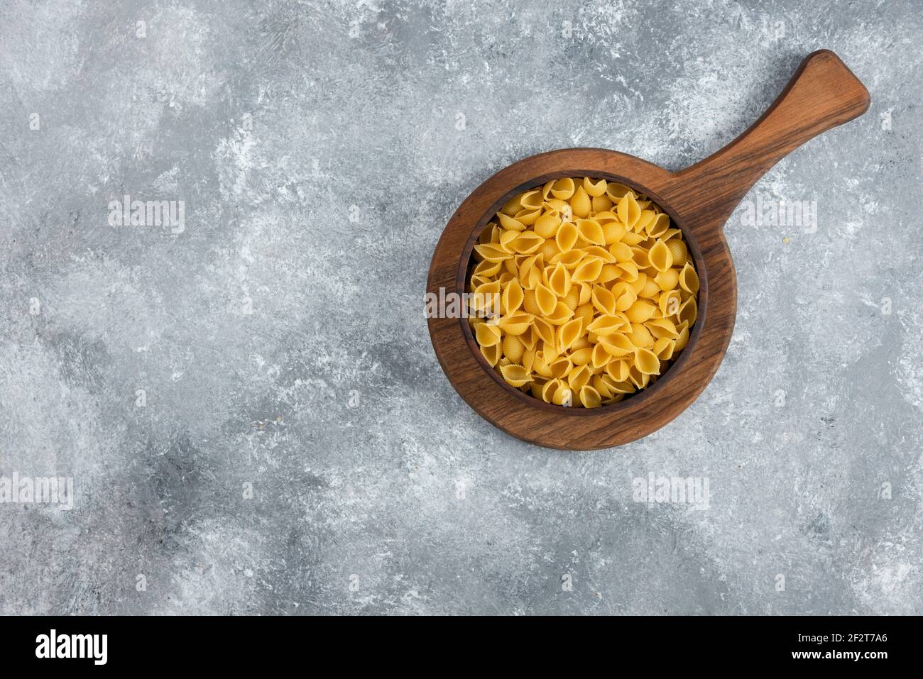 Wooden bowl of raw seashell pasta on cutting board Stock Photo