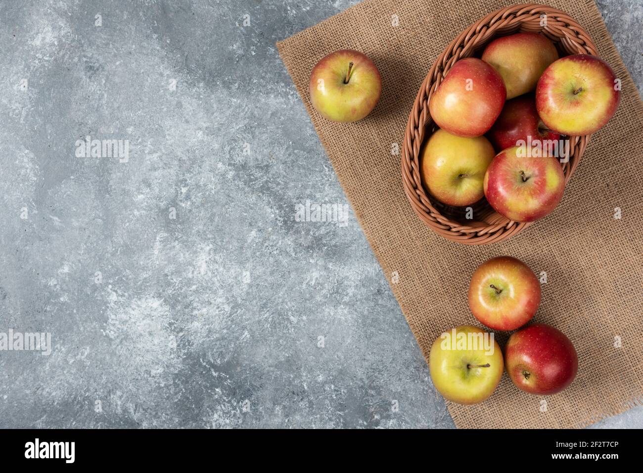 Wicker basket of ripe shiny apples on marble surface Stock Photo