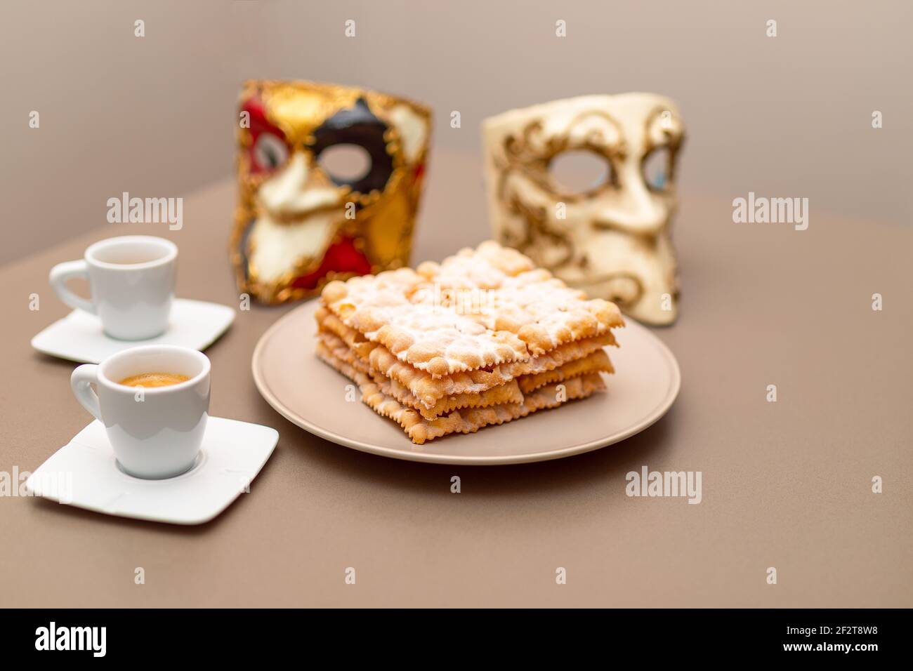 Typical Italian carnival fritters (Chiacchiere di Carnevale) dusted with powdered. Composition with two cups of coffee and in the background are Venet Stock Photo