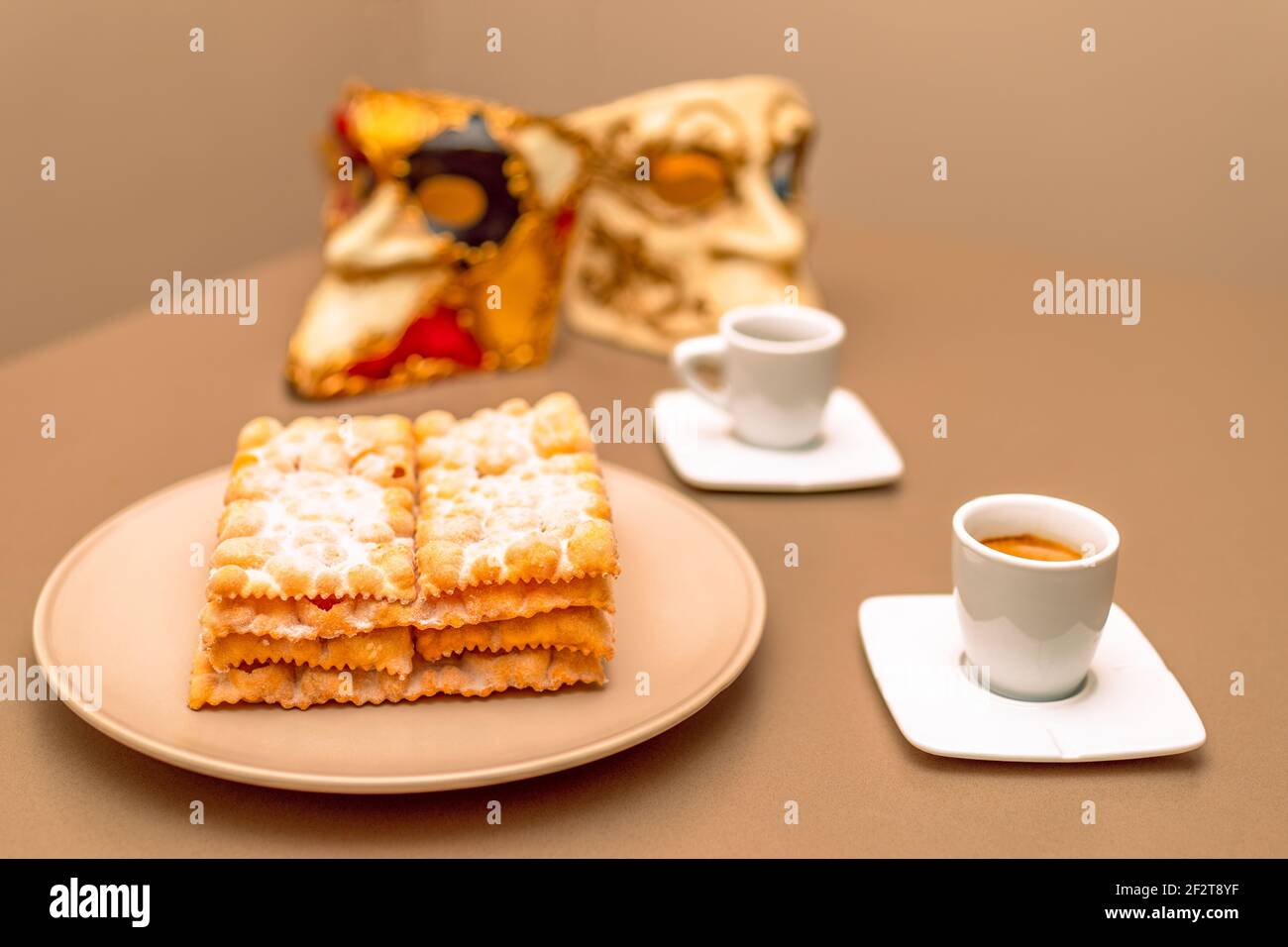 Typical Italian carnival fritters (Chiacchiere di Carnevale) dusted with powdered. Composition with two cups of coffee and in the background are Venet Stock Photo