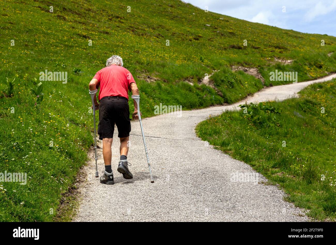 a senior with crutches during his rehabilitation on a mountain slope Stock Photo