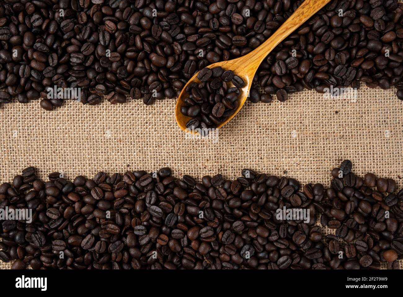 Pile of medium roasted coffee beans with wooden spoon scattered on burlap Stock Photo