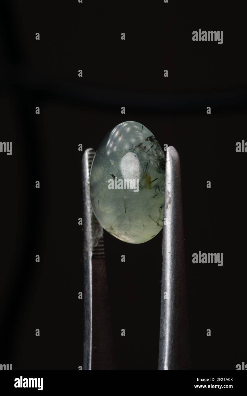 Natural prehnite stone in tweezers on a black background Stock Photo
