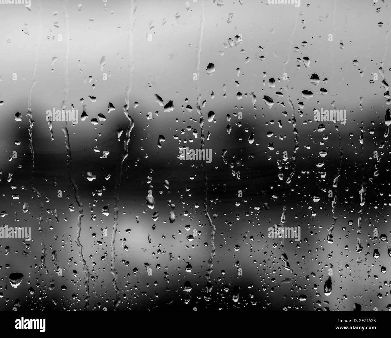Monochrome image of Raindrops on window with the soft focus hillside terrace of suburban housing beyond Stock Photo