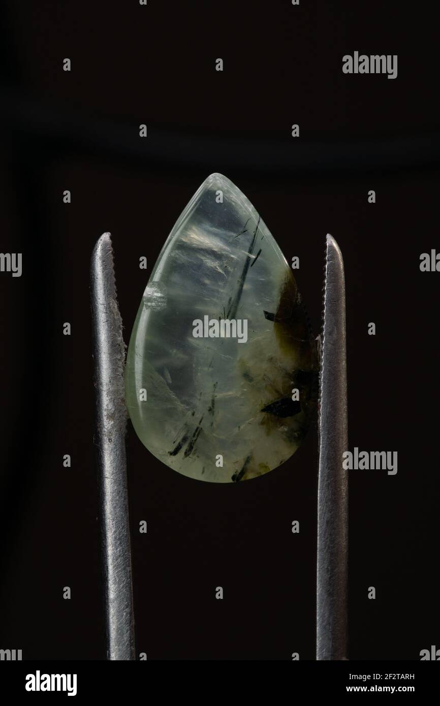 Natural prehnite stone in tweezers on a black background Stock Photo