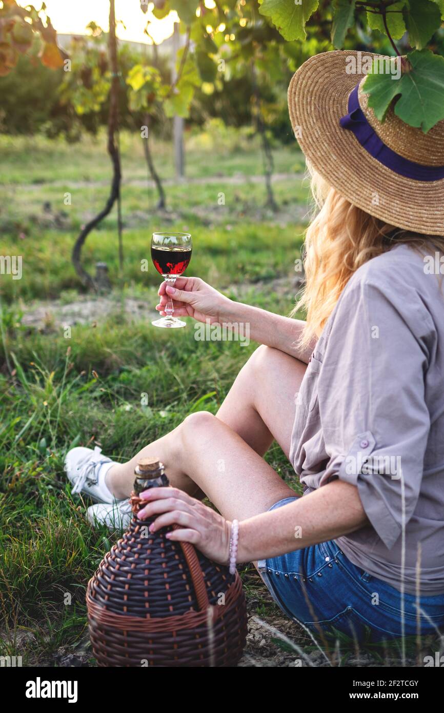 Woman tasting red wine in vineyard. Young farmer drinking homemade wine outdoors. Enjoyment of life Stock Photo