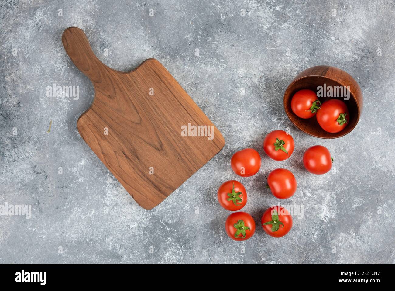 Wooden bowl of red tomatoes with cutting board on marble background Stock Photo