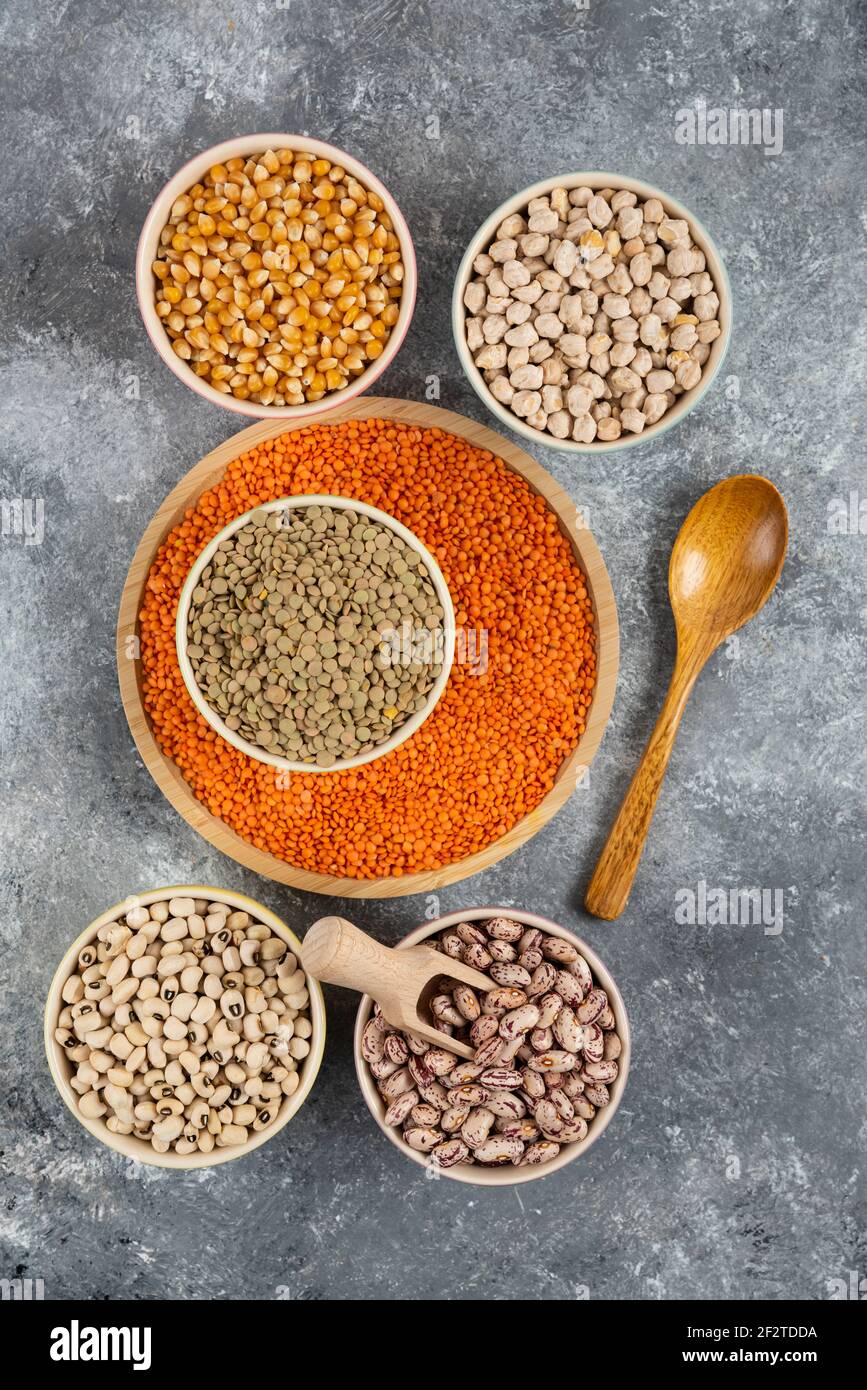 Bowls of various uncooked beans, lentils and corns on marble surface Stock Photo