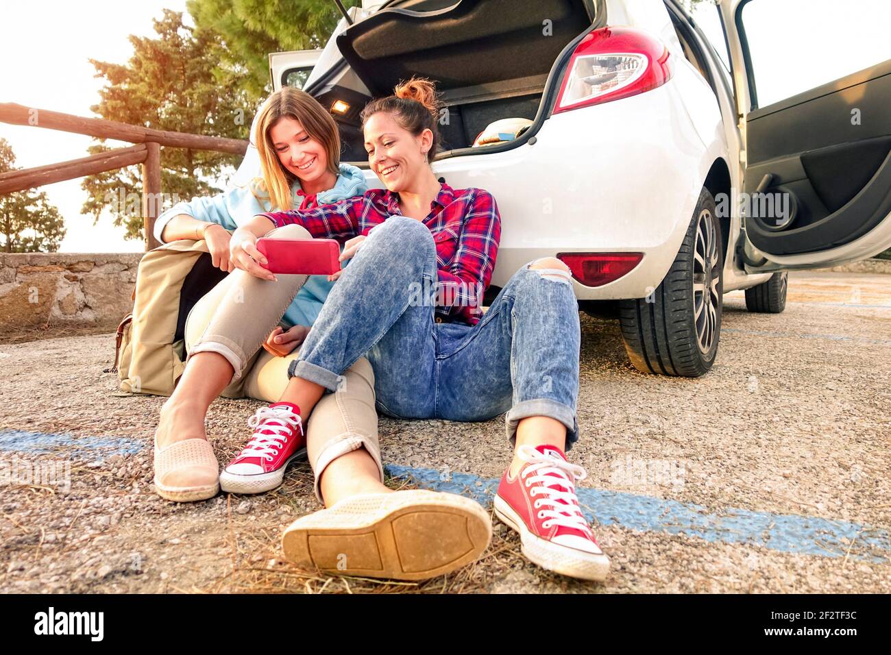 Young female best friends having fun with mobile smart phone at car trip moment - Wanderlust concept during happy travel vacation on the road Stock Photo