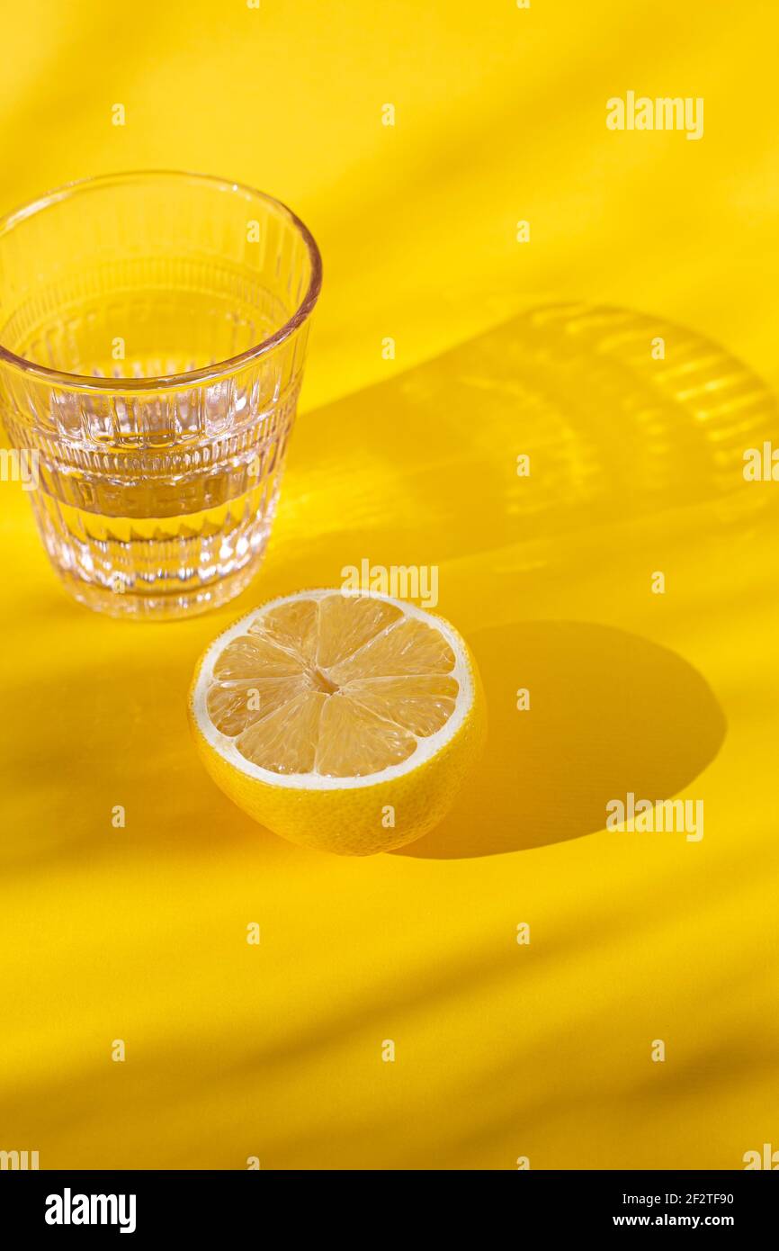 White Crystal class with lemon on a white or yellow surface, for healthy and holistic living Stock Photo