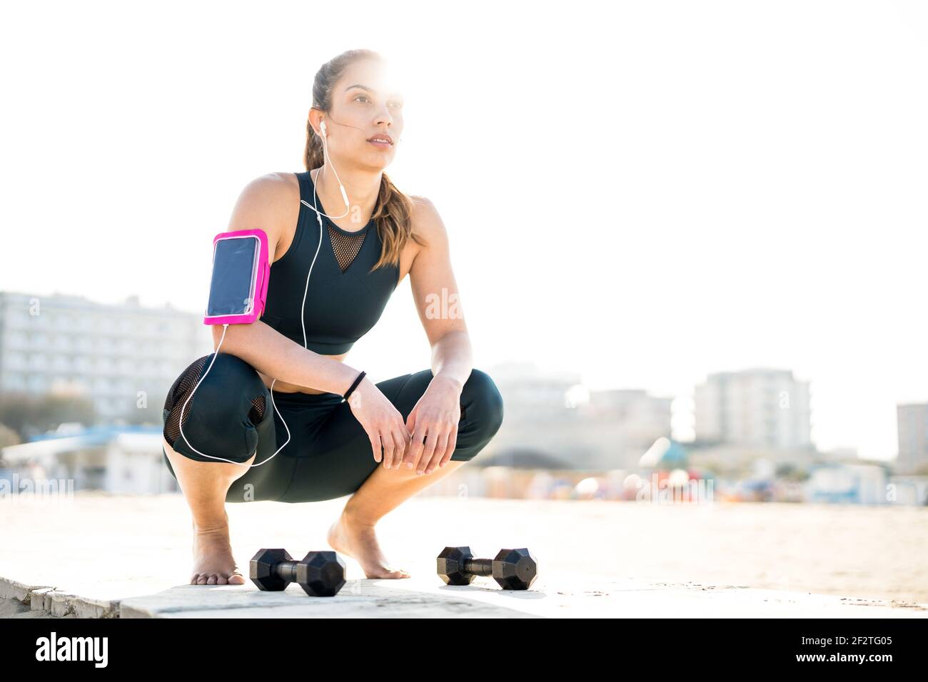 Portrait of athletic woman on a break moment listening music at outdoors beach location - Modern alternative work out and body care concept Stock Photo