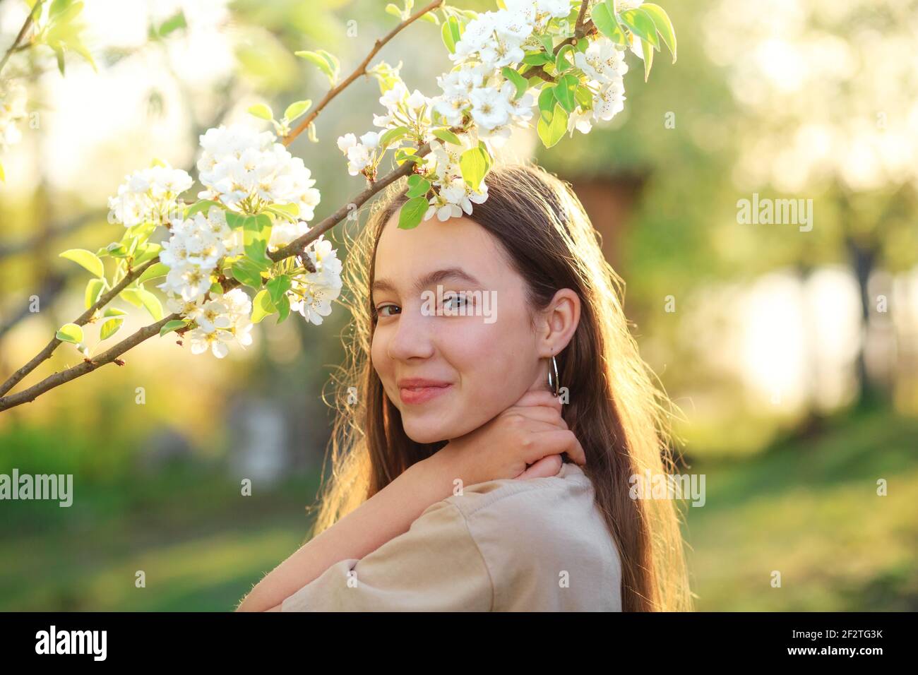 Beautiful teenager girl with blooming apple flowers. Happy cute kid having fun outdoors at sunset. Stock Photo