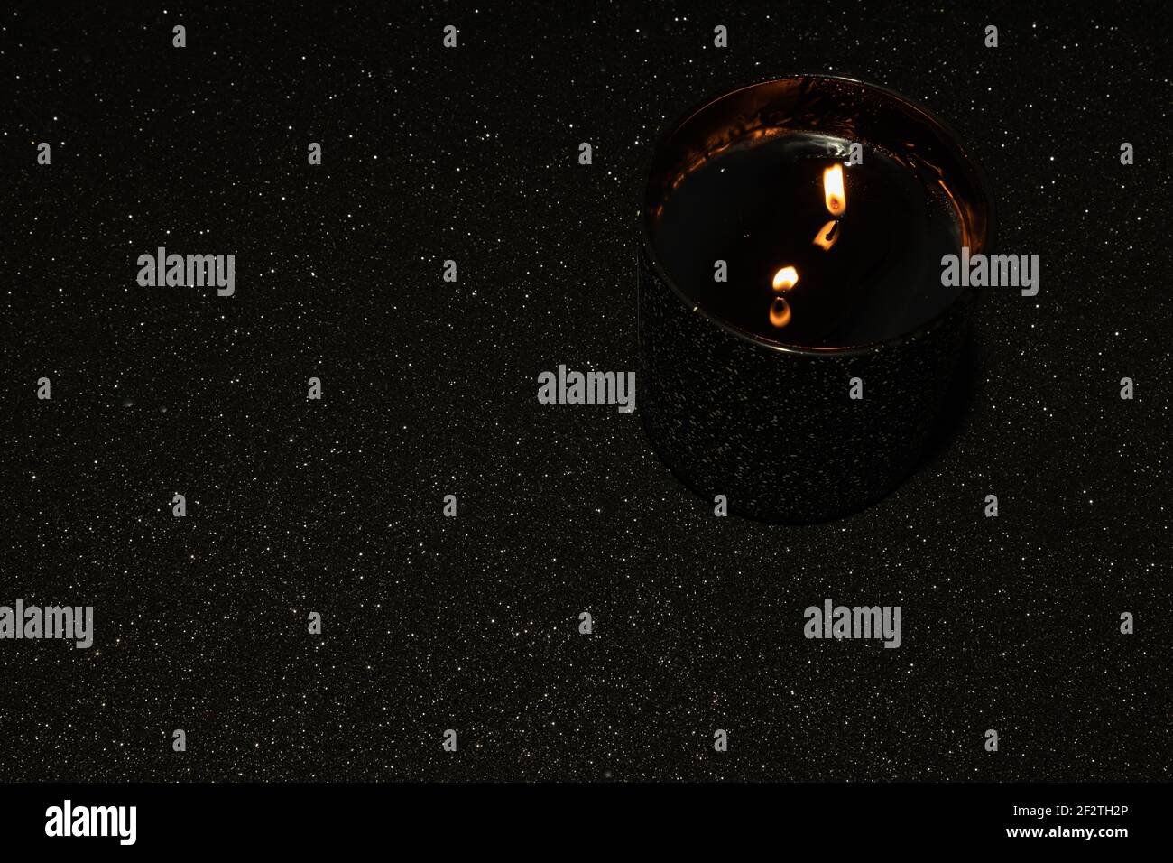 Black lighted candle with two wicks on a black background with sparkles