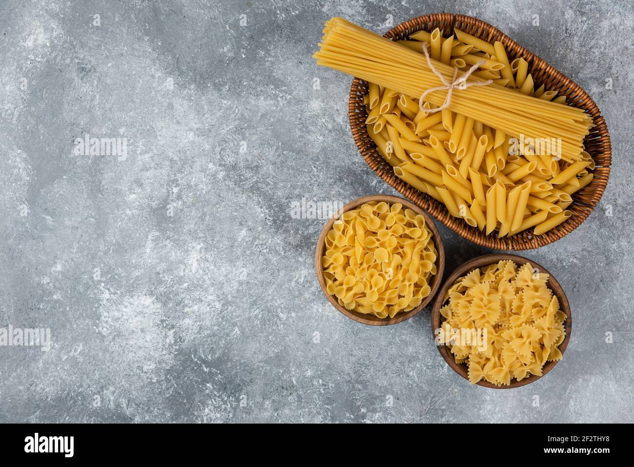 Pile of various uncooked dry pasta in wicker basket and wooden bowls Stock Photo