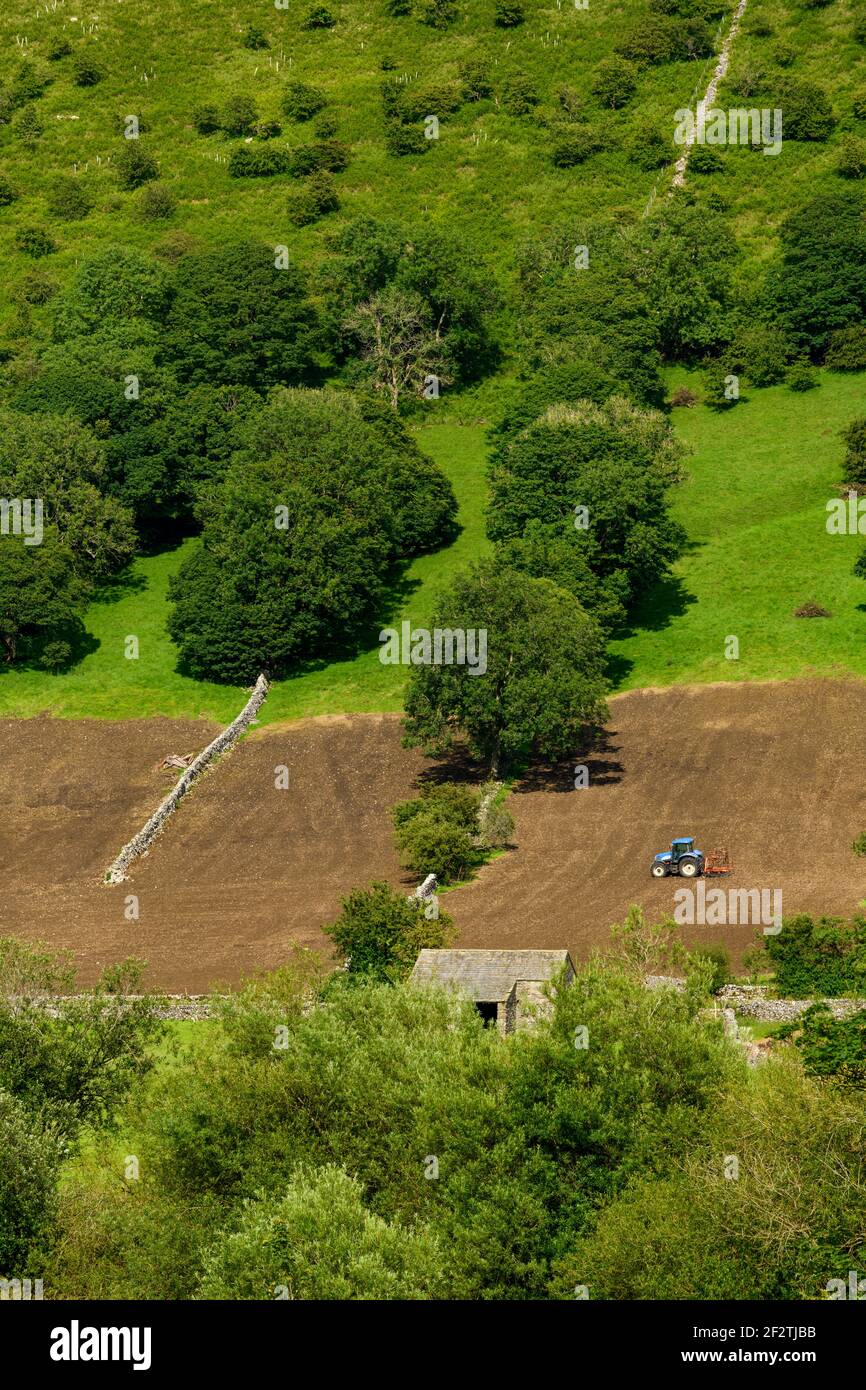 Tractor working on high slopes of scenic steep-sided hillside field (tilling harrowing soil for seeding) - Wharfe Valley, North Yorkshire, England UK. Stock Photo