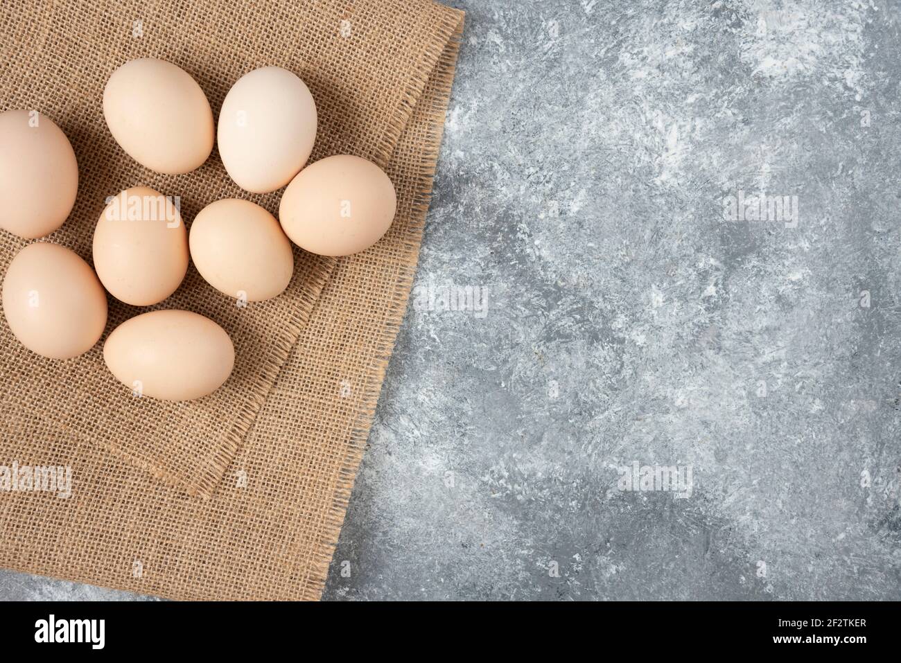 Raw organic eggs placed on top of sackcloth on marble background Stock Photo