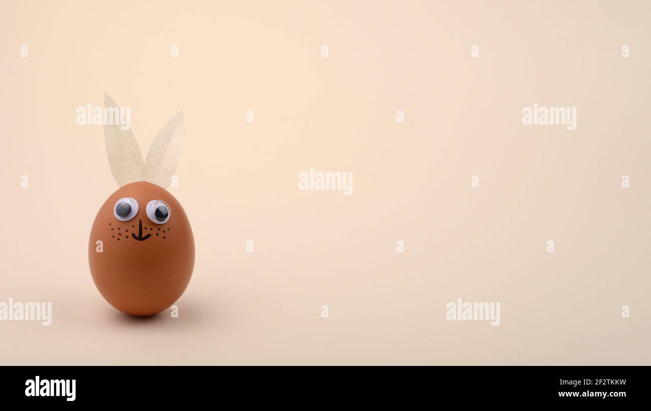 One Easter egg with eyes and rabbit ears on beige horizontal background. Copy space. Happy Easter concept. Stock Photo