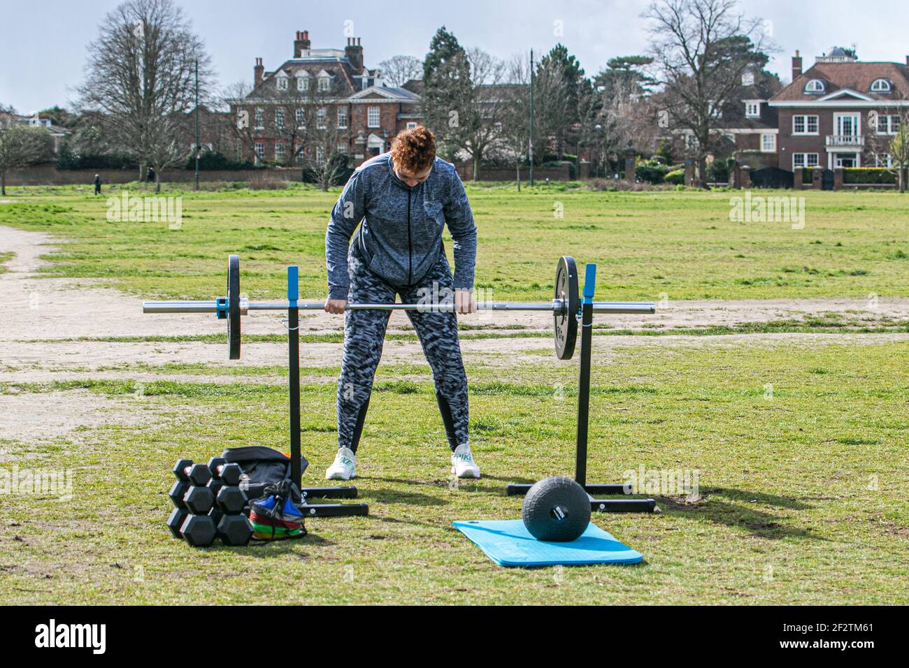 WIMBLEDON LONDON, UK 13 March 2021.  Cara exercises outdoors using weights is watched by her trainer Matthew on Wimbledon Common during lockdown on a cold blustery day. The government has started to relax lockdown restricitons allow people to meet and exercise outdoors as part of the roadmap to get back to normal life Credit amer ghazzal/Alamy Live News Stock Photo