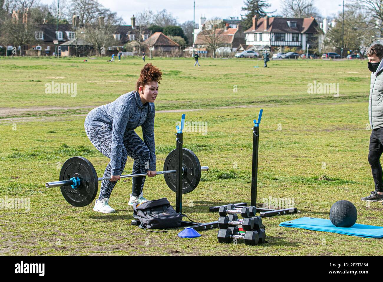 WIMBLEDON LONDON, UK 13 March 2021.  Cara exercises outdoors using weights is watched by her trainer Matthew on Wimbledon Common during lockdown on a cold blustery day. The government has started to relax lockdown restricitons allow people to meet and exercise outdoors as part of the roadmap to get back to normal life Credit amer ghazzal/Alamy Live News Stock Photo