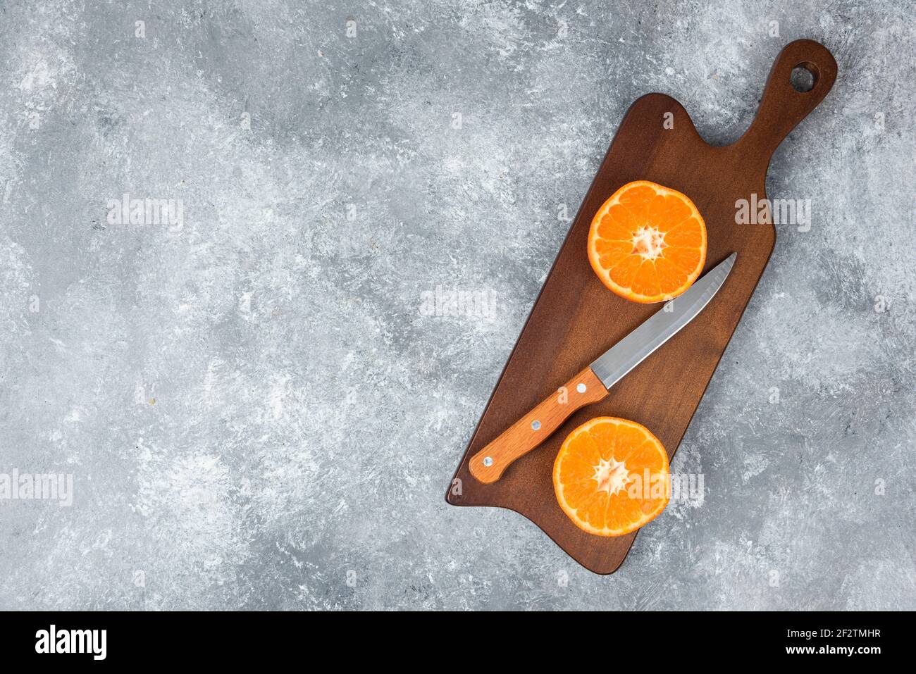 A wooden board of juicy slices of orange fruit with a knife on stone background Stock Photo