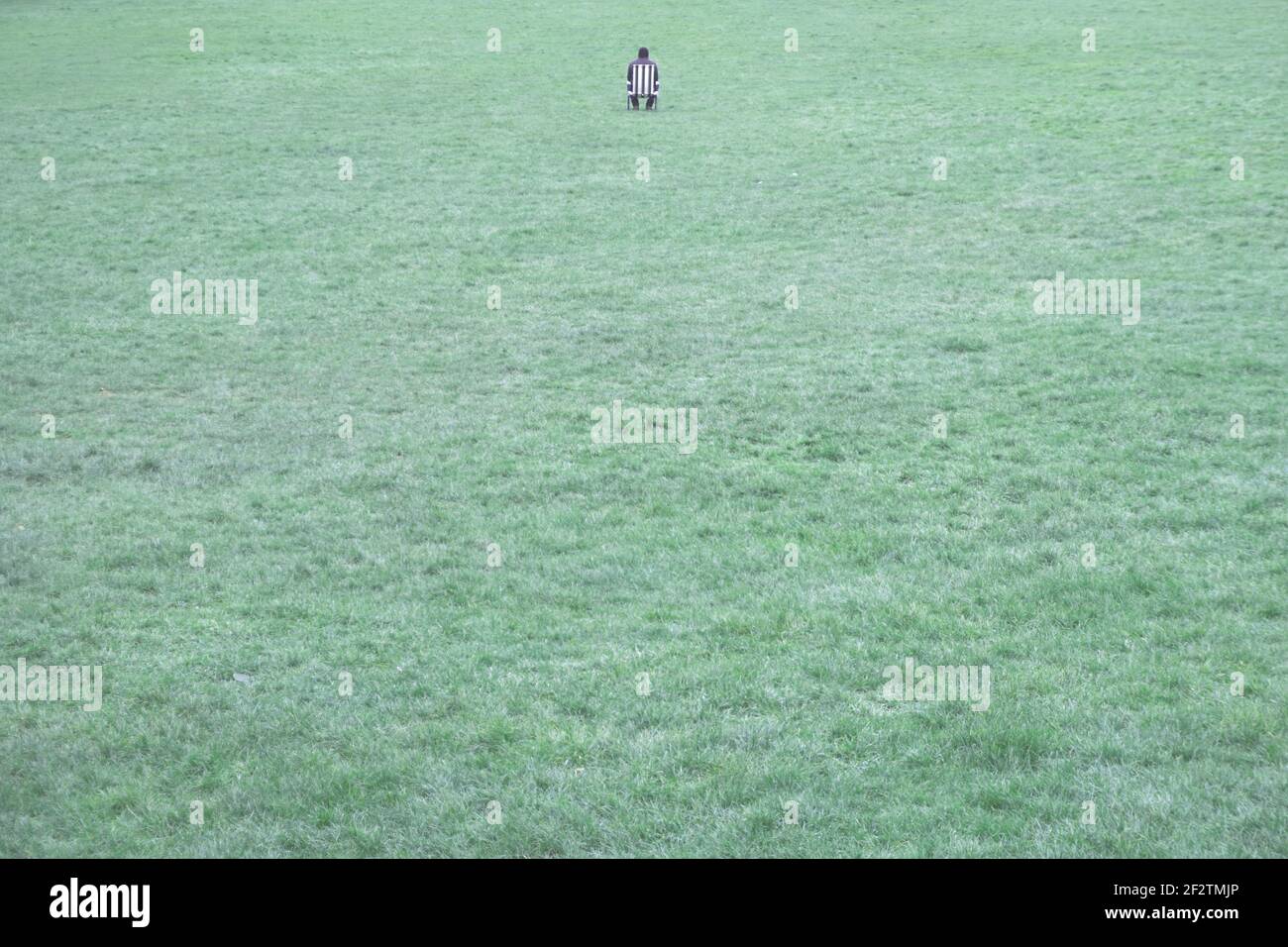 Portraying contemplation and solitude, a man sits alone on a deck chair in the middle of a field in Richmond Park, London, UK Stock Photo