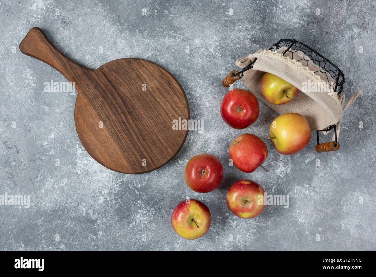 Bunch of fresh ripe apples out of wicker basket on marble surface Stock Photo