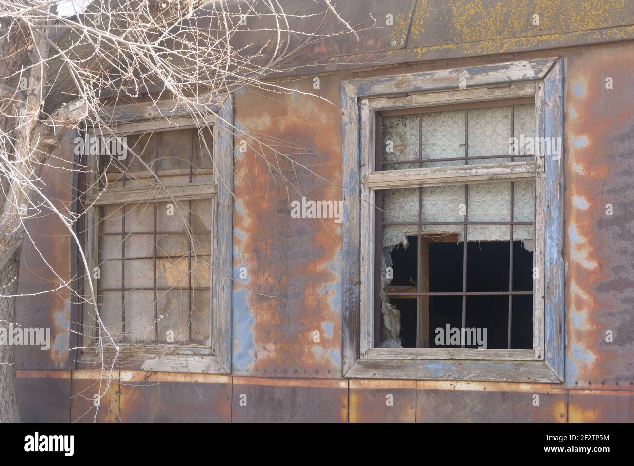 Old windows with iron bars on facade of abandoned caravan building. Rust and peeling paint on walls of facade. Stock Photo