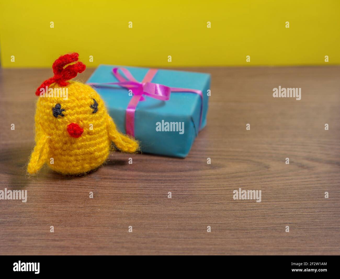 Toy yellow chicken next to gift in blue wrapper on brown table. Stock Photo