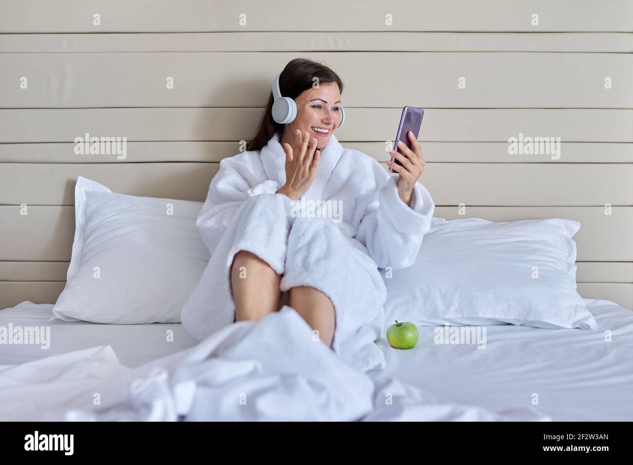 Happy talking mature woman in headphones using smartphone for video ...