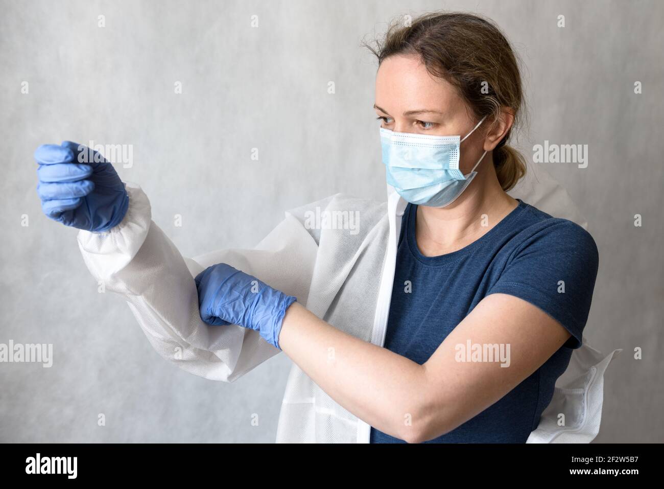 Doctor puts on personal protective equipment (PPE) due to COVID-19, female nurse with medical coverall for coronavirus, woman physician holds uniform Stock Photo