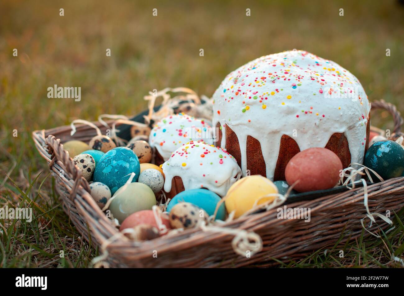 Wicker basket with Easter cake and eggs on green grass background Stock Photo