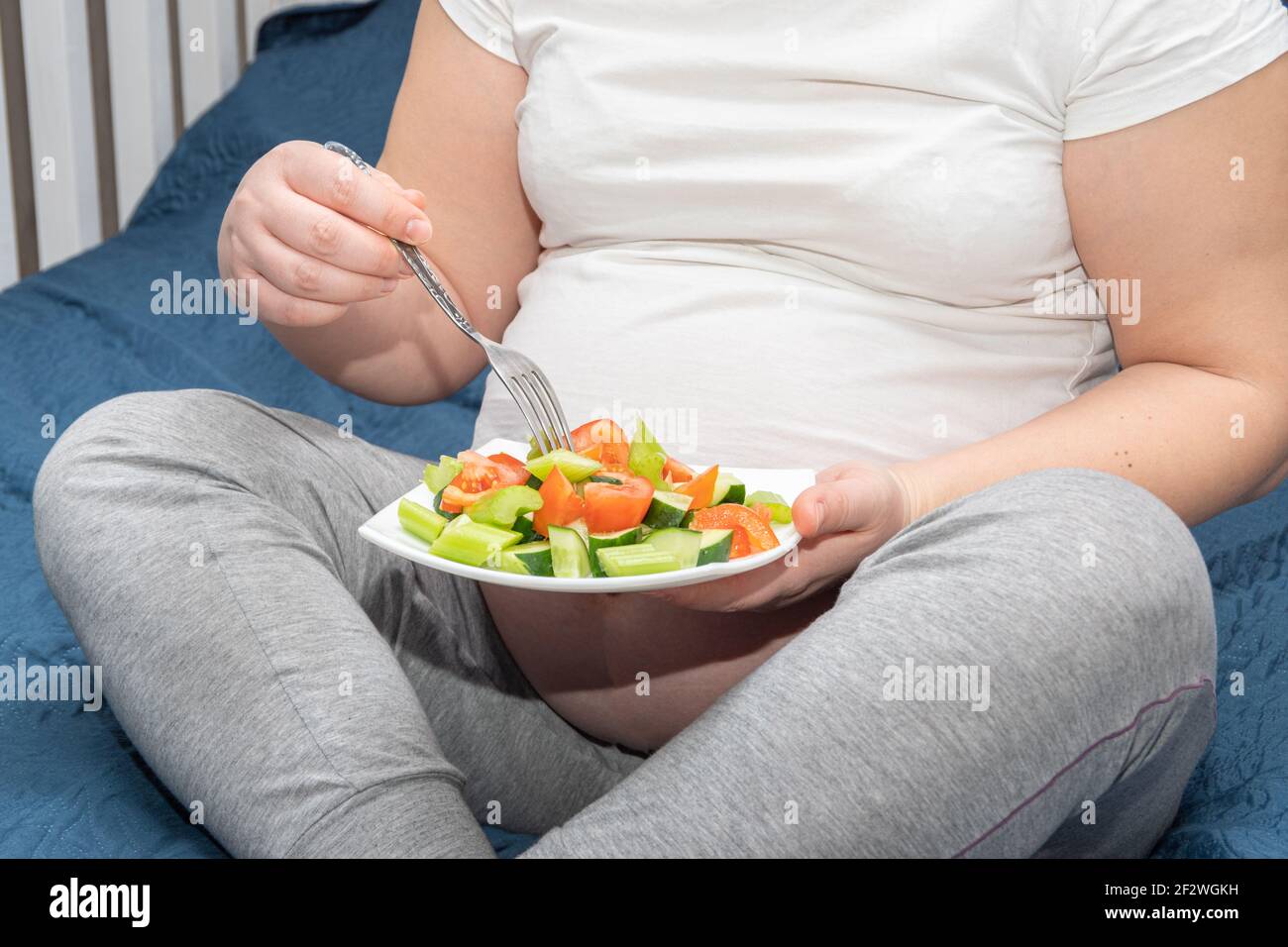 A pregnant woman is eating a healthy homemade organic fruit salad while sitting on her bed