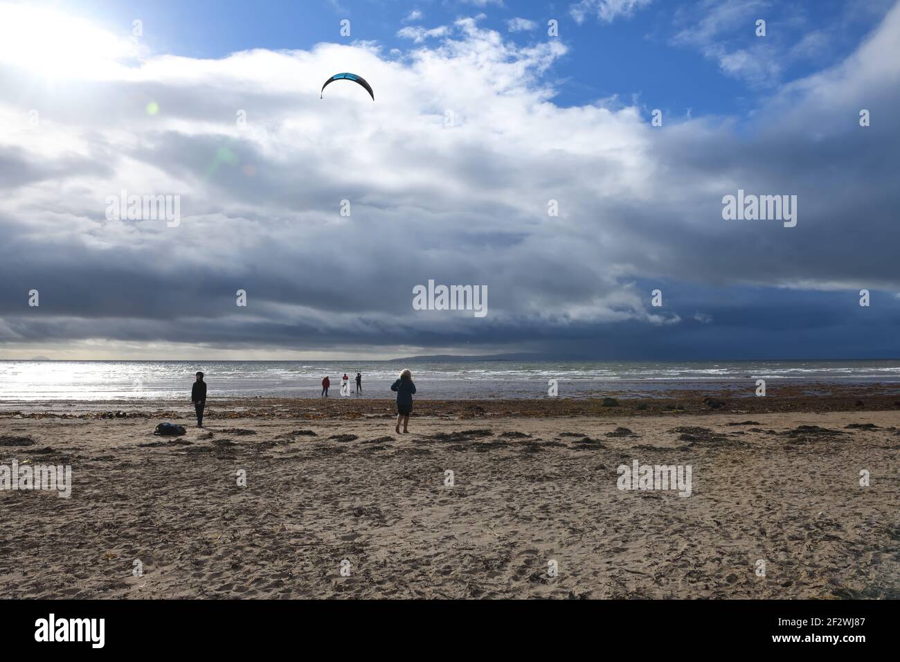 Troon, Ayrshire, Scotland, UK. 13th, March, 2021. A kite surfer prepares to take advantage of a strong on shore winds at Troon beach as dark rain clouds move quickly overhead. Credit. Alamy Live News/ Douglas Carr Stock Photo