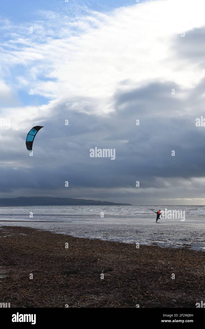 Troon, Ayrshire, Scotland, UK. 13th, March, 2021. A kite surfer prepares to take advantage of a strong on shore winds at Troon beach as dark rain clouds move quickly overhead. Credit. Alamy Live News/ Douglas Carr Stock Photo
