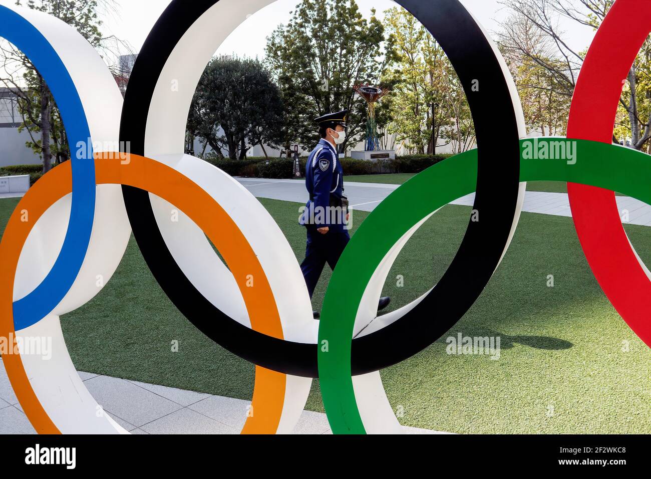 a-man-wearing-a-facemask-walks-behind-the-olympic-symbols-of-the-five