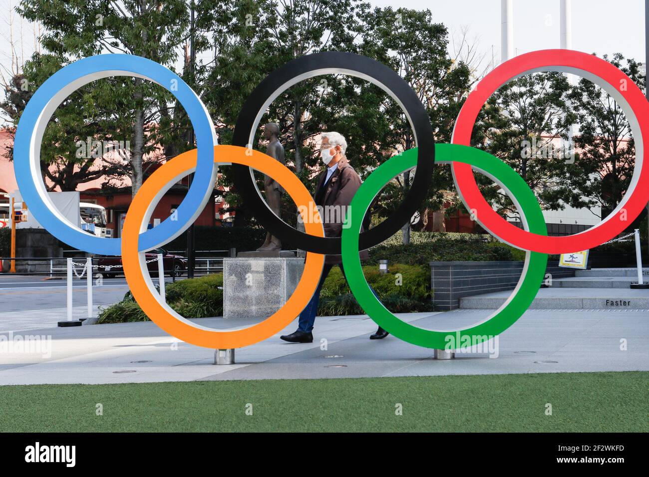 a-man-wearing-a-facemask-walks-behind-the-olympic-symbols-of-the-five