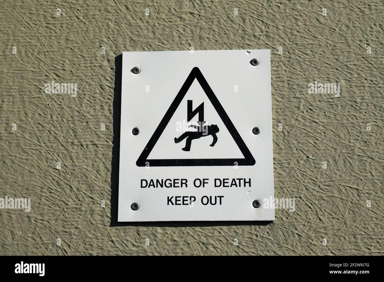 Danger of death keep out sign with icon of person being electrocuted in warning triangle. isolated against neutral coloured wall. Stock Photo