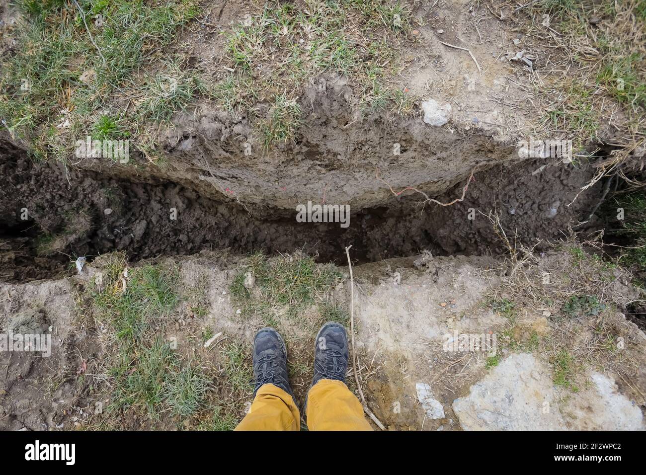 Large crater in the ground after a strong earthquake of magnitude 6.2., which was 2 months ago. Comparison of human legs with crater size. Stock Photo
