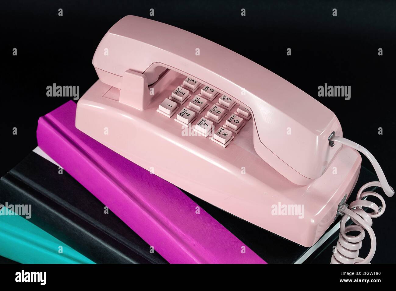 Close up of retro pink telephone on a stack of hardcover books isolated on black Stock Photo