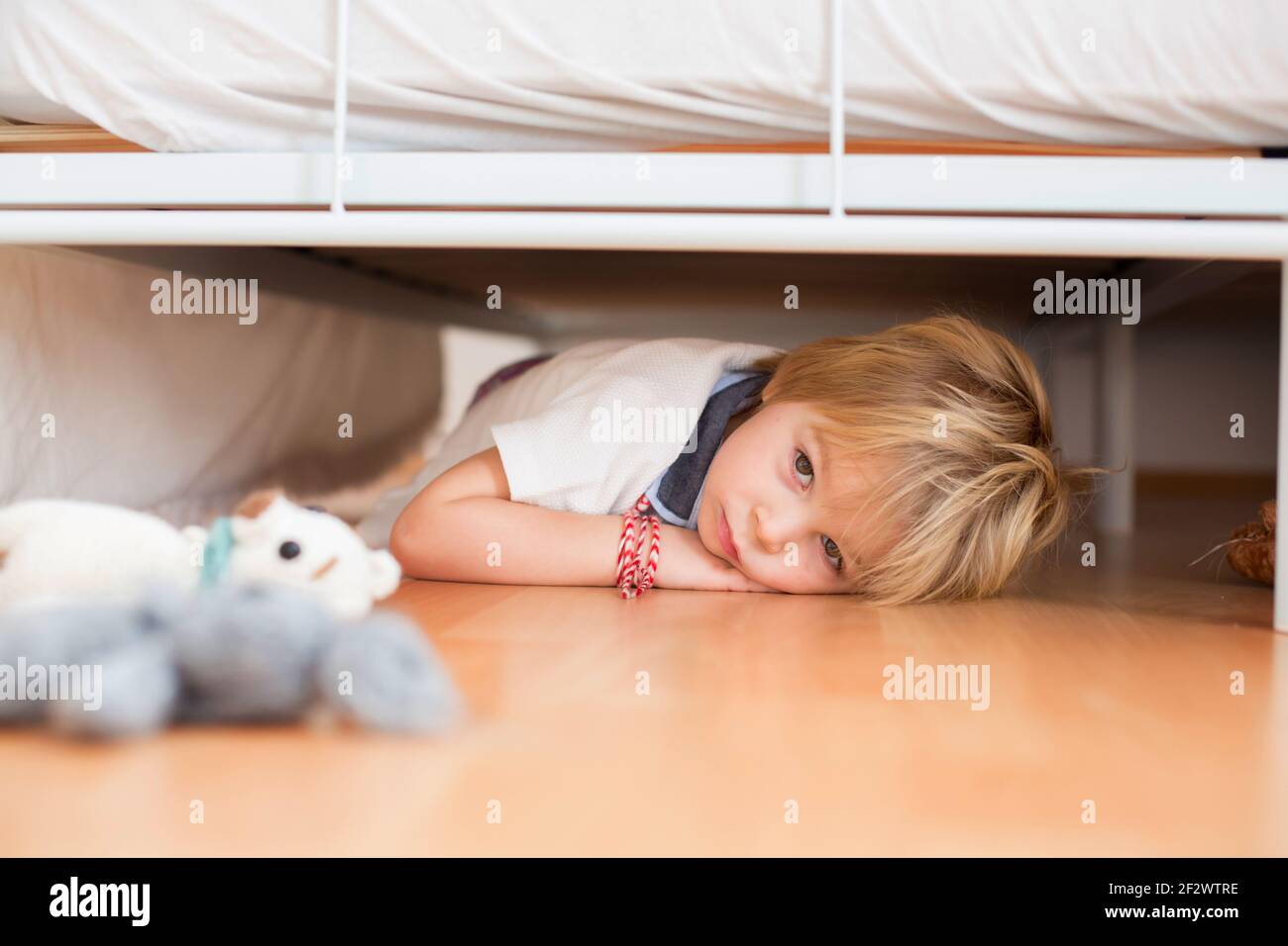 Little toddler child, hiding under the bed with stuffed toys, scared