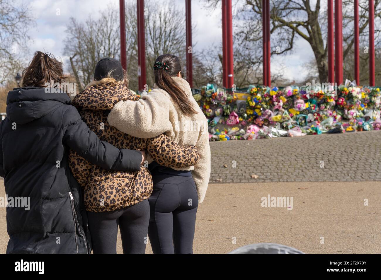 back view of three women cuddle together to pay  floral tributes at Clapham Common bandstand in memory of Sarah Everard,, London, England Stock Photo