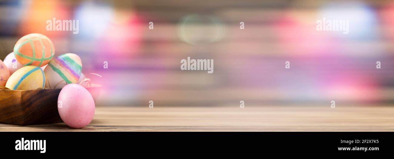 Colorful easter eggs on a wooden plate on a table on a pink background. Stock Photo
