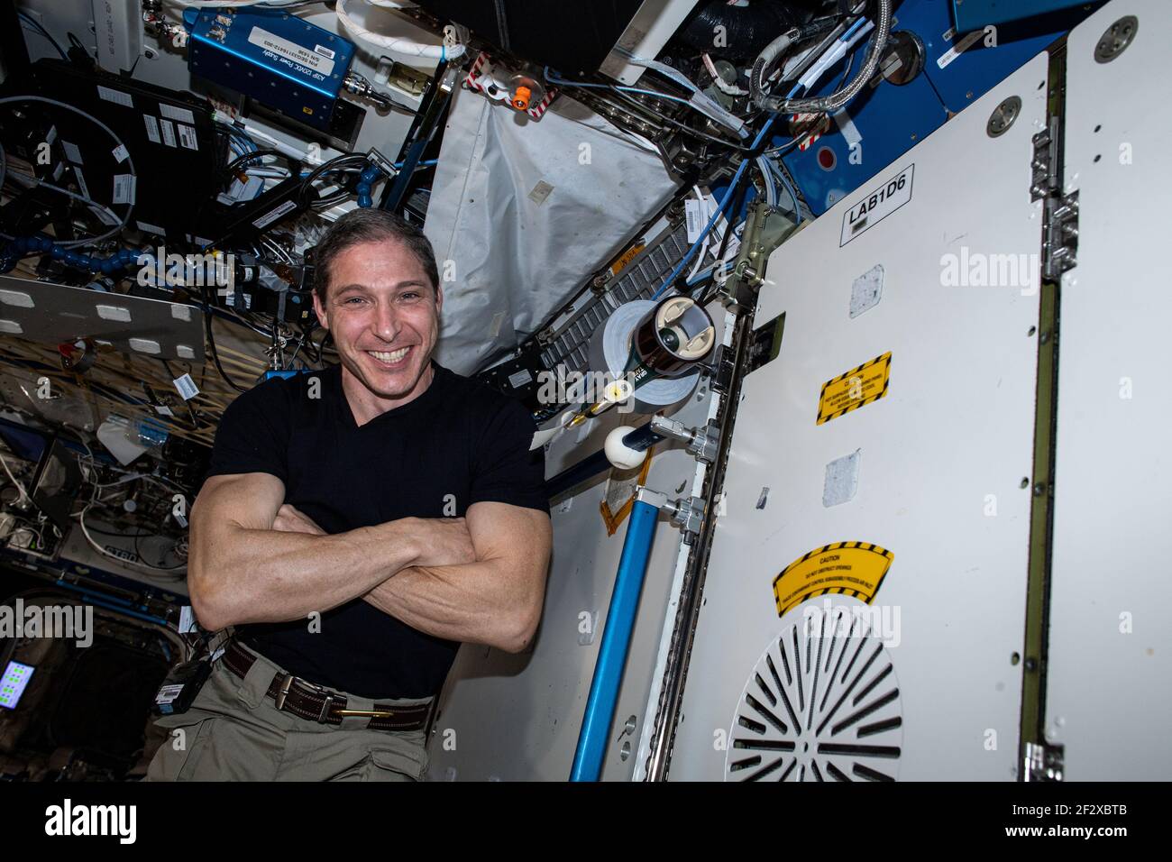 NASA astronaut and Expedition 64 Flight Engineer Michael Hopkins smiles as he poses next to a tape dispenser created by high school students united with NASA to create hardware aboard the International Space Station March 4, 2021in Earth Orbit. Stock Photo