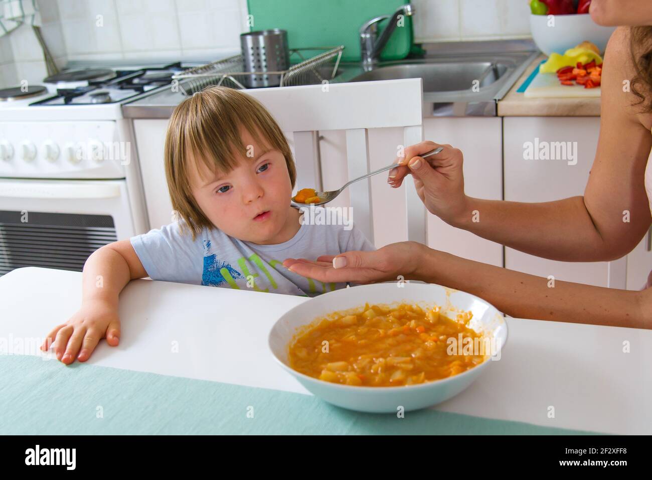 Boy with down syndrome refuses healthy food given by his mother. Stock Photo