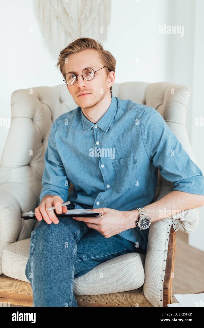 Portrait of serious caucasian man psychologist sitting in armchair at the workplace, holding a
