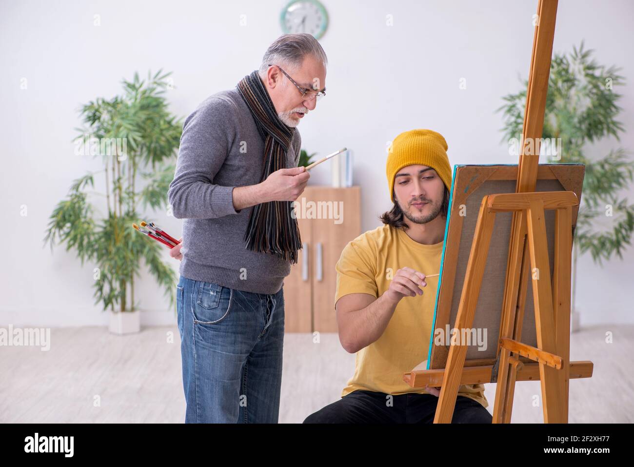 Young man taking lesson from experienced painter Stock Photo